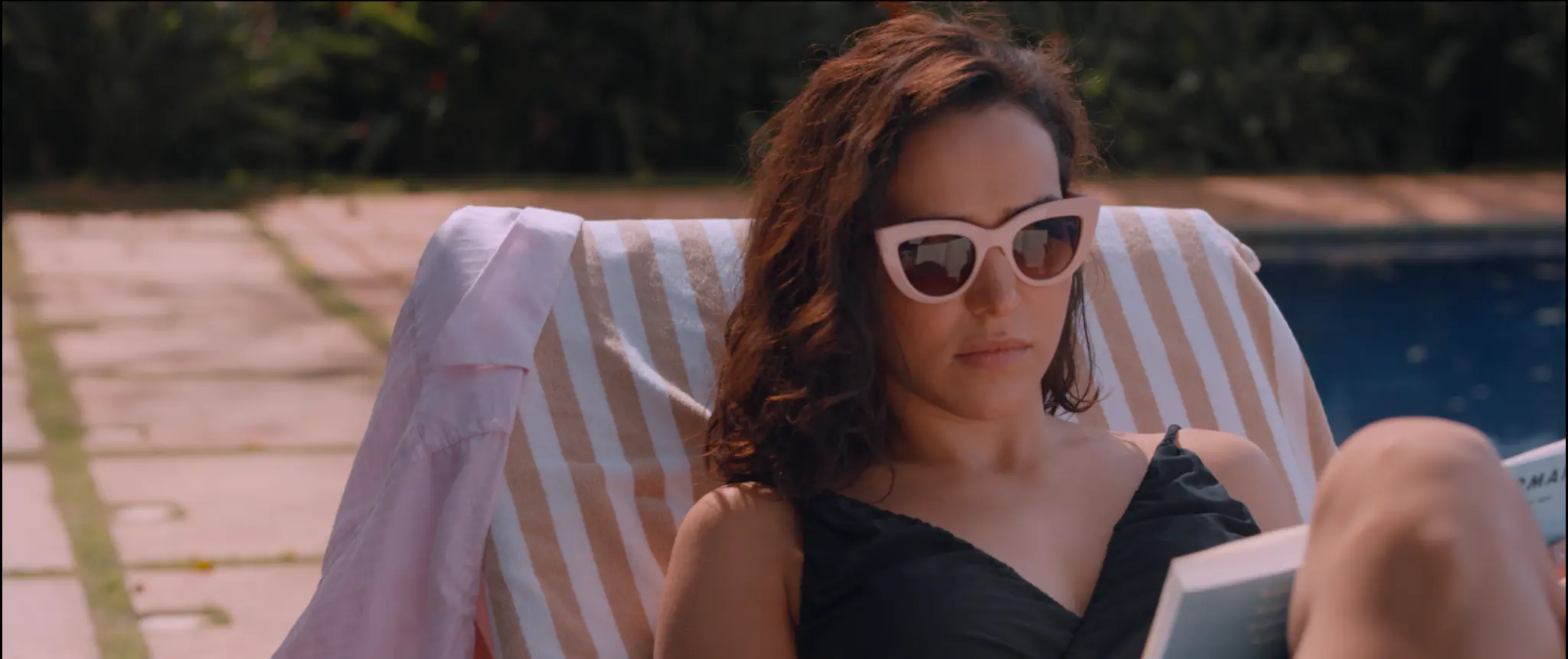 Mulher de óculos escuros lê junto à piscina