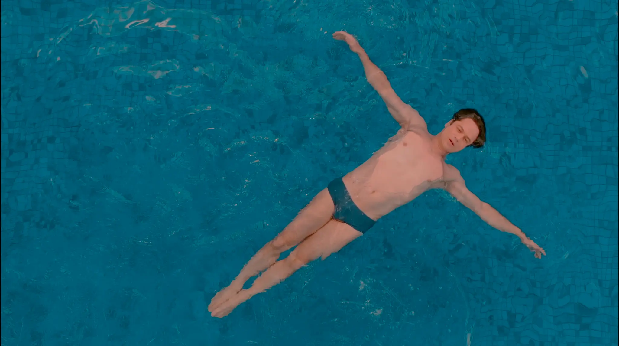 Homem flutua de braços abertos em uma piscina azul