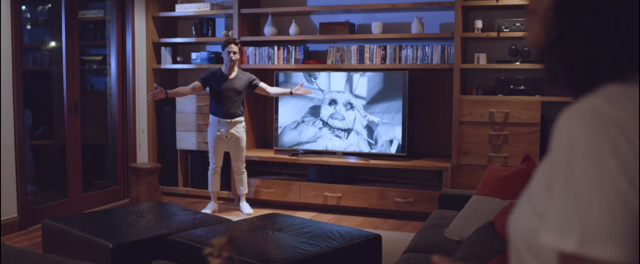 Homem gesticula diante de uma televisão em uma sala