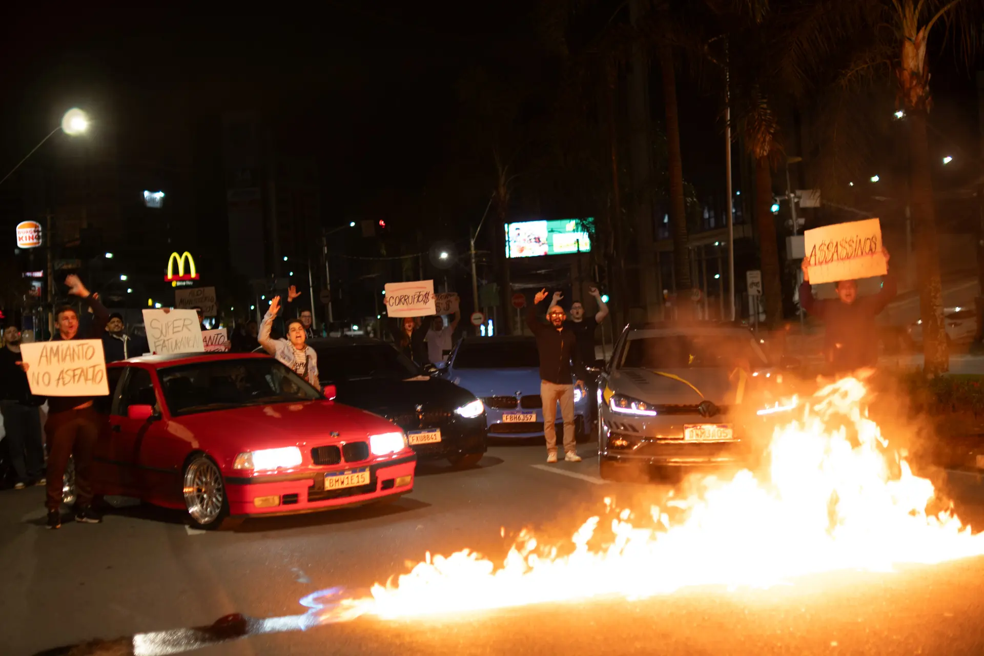 Cena de Asfalto com carros, manifestantes e fogo