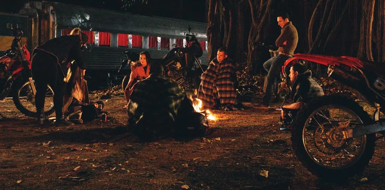 Elenco reunido entre motos e carros ao redor de uma fogueira