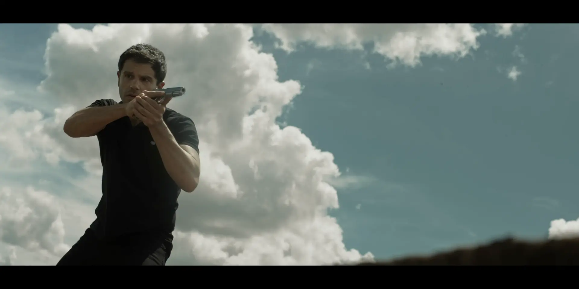John segura uma arma sob o céu aberto